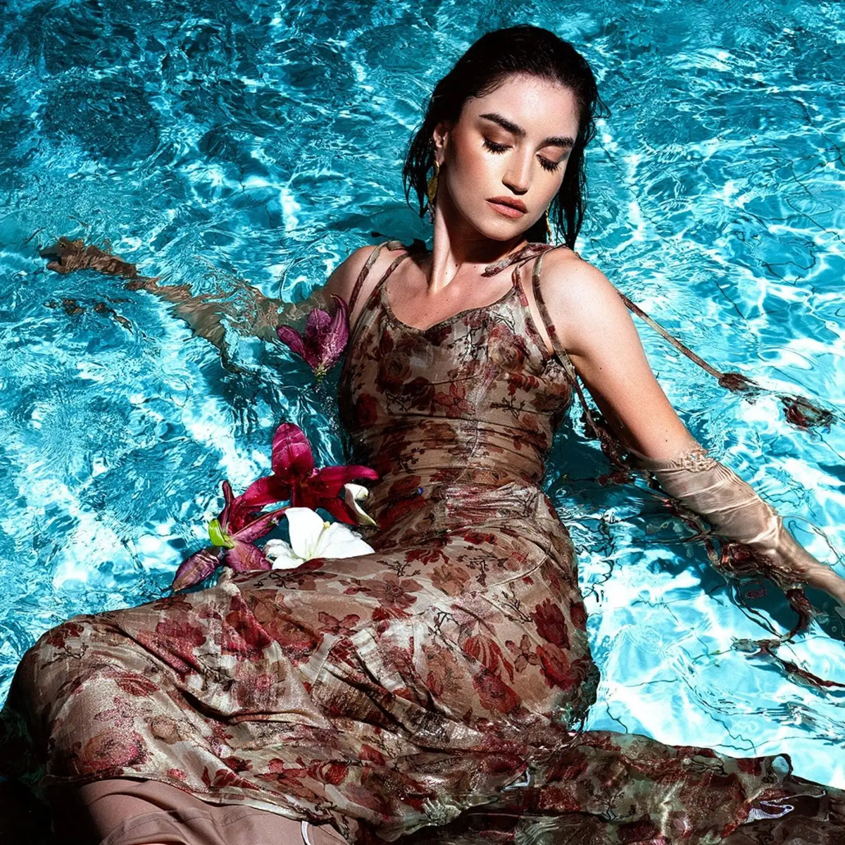 A flowing, earth-toned floral dress with delicate straps and a shimmering satin-like texture.