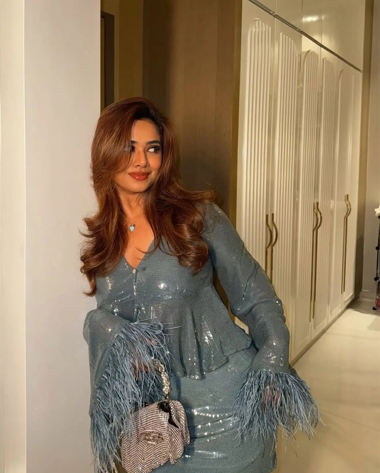 A shimmering light blue sequined dress with feathered cuffs and a ruffled neckline.