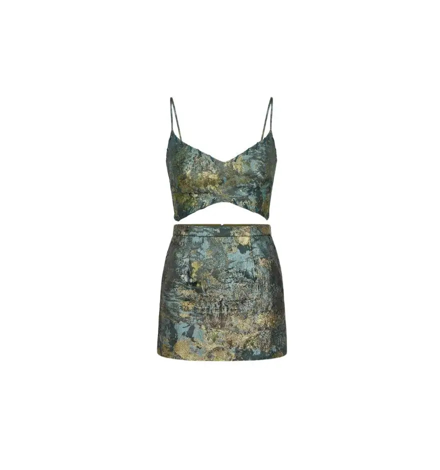 A two-piece set featuring a cropped top with thin straps and a matching mini skirt, both adorned in an abstract, textured pattern of muted greens, blues, and golds.