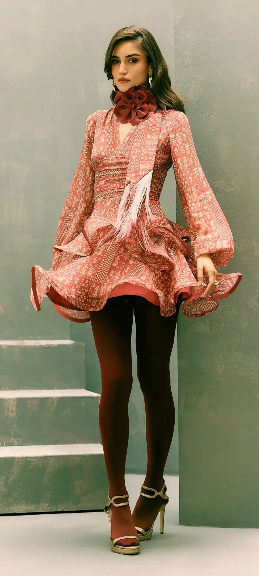 A woman wears a pink patterned dress with ruffled sleeves and hem, accented by a matching floral collar.